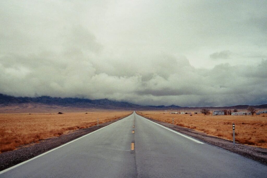 A lonely country road in the Nevada desert under a cloudy sky, an exploration of liminal spaces and visual abstraction.
